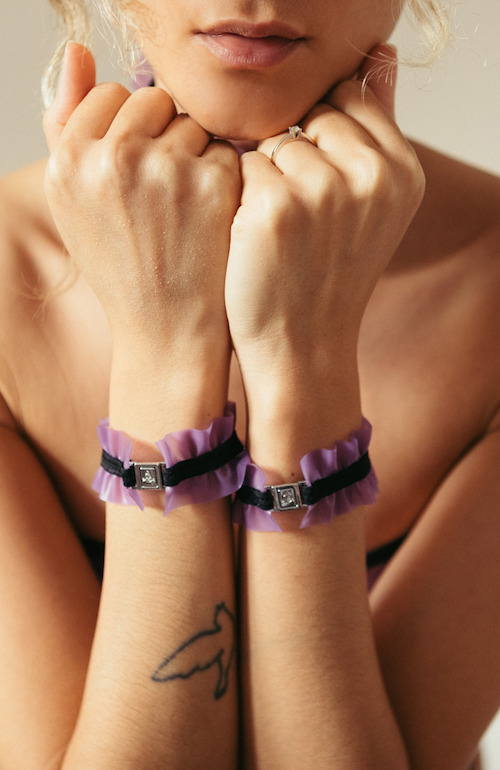 Lencería de látex hecha a mano. El top tiene forma de bandeau y una abertura en la espalda para ajustar la talla. La braguita es un sencillo tanga triangular con un pequeño triángulo en la parte inferior. El conjunto de lencería también incluye una especie de liguero (alrededor de las caderas) con tiras que bajan hasta las piernas y a las que se sujetan unos tirantes rizados de látex. También hay un collar y un brazalete rizados