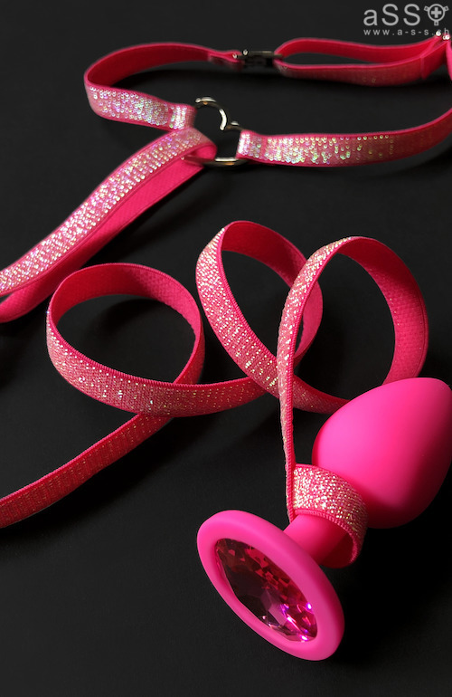 Lencería hecha a mano con tirantes elásticos de color metálico. La lencería es de una sola pieza y llega hasta el cuello. La parte delantera del cuello tiene un pequeño corazón de metal grabado con la inscripción «Love your aSS». En la parte inferior, la lencería se sujeta con un plug anal. Todas las correas son ajustables.