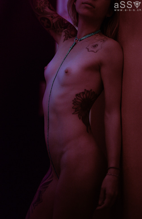 Lencería hecha a mano con tirantes elásticos de color metálico. La lencería es de una sola pieza y llega hasta el cuello. La parte delantera del cuello tiene un pequeño corazón de metal grabado con la inscripción «Love your aSS». En la parte inferior, la lencería se sujeta con un plug anal. Todas las correas son ajustables.